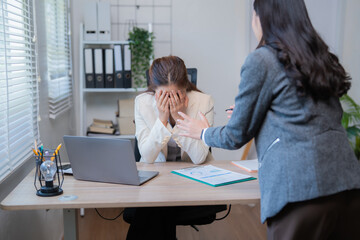 Business woman is stressed and covering her face with hands while manager is scolding her about...