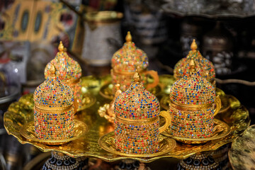 Ornate Turkish coffee sets adorned with colorful jewels displayed on golden trays at a bustling...