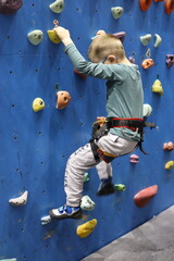 Five-year-old boy climbing an indoor climbing wall, focused and determined as he navigates colorful handholds