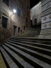 A section of the back view of Siena's Duomo and the staircase at piazza San Giovanni under a light night rain. Travel to Tuscany, Italy.