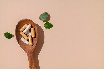 Vitamins, capsule, nutraceutical, food supplement in wooden spoon on beige background top view....