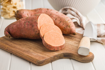 Raw sweet potatoes on cutting board on white table.