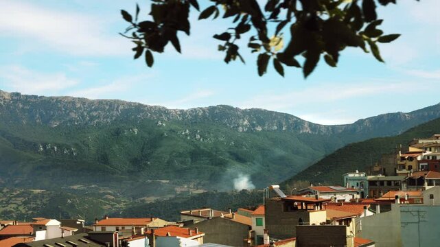 Mountainous terrain embraces Orgosolo, Sardinia, in Italy, with the village nestled among rugged peaks. Leaves in the foreground create a natural vignette around this peaceful landscape.