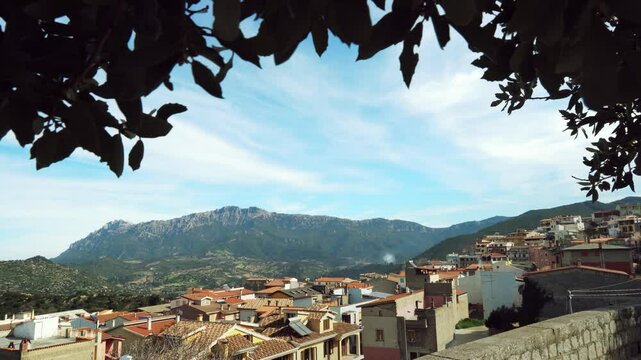 Landscape view of the municipality of Orgosolo, Sardinia in Italy. Leaves in the foreground frame the scene, creating a natural vignette around this Italian town.
