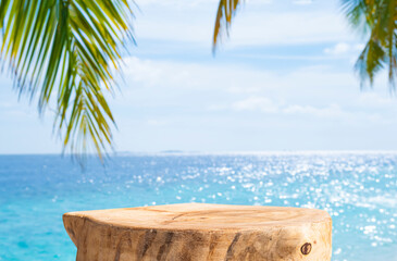 Stump table on beach with blurred blue sea, sky and green palm leaves background
