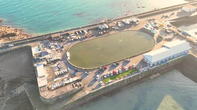 Guernsey St Peter Port.Dropping overhead drone footage of model yacht pond on bright sunny afternoon with clear blue sea,Guernsey Yacht Club and boats on hardstanding