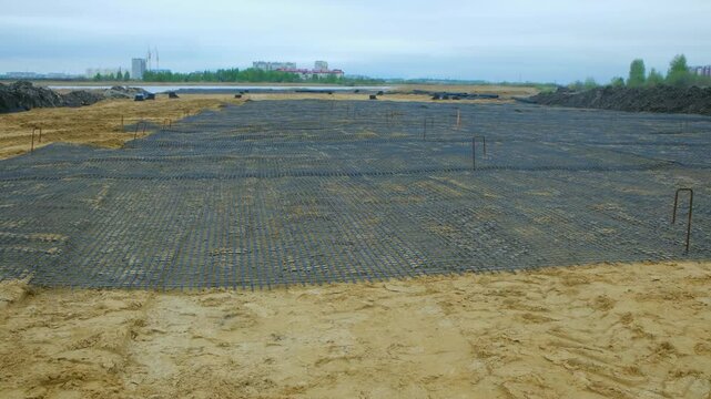 Laying a geogrid on a sand base to prepare for asphalt paving, ensuring stability and preventing future road damage. Laying geogrid for road construction. Construction of a future asphalt road.