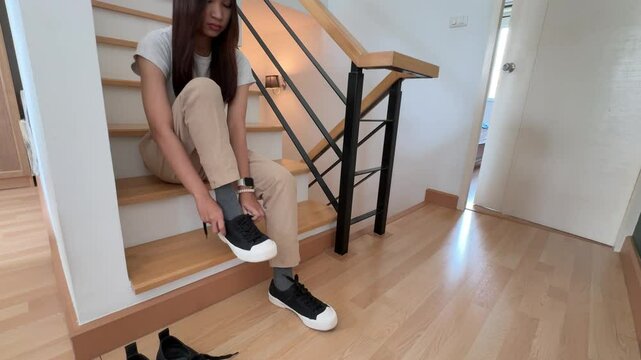 The Southeast Asian teenage girl is wearing socks and shoes on the stairs at home.