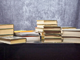 Stack of books resting on a black desk. Behind the desk a white background
