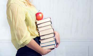 Close-up of female hands holding a stack of books and a red apple. The woman is carrying many books...