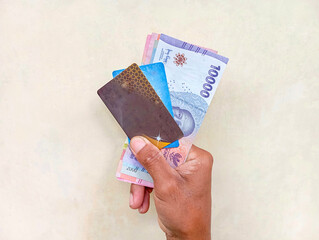 hands holding rupiah notes and credit cards
