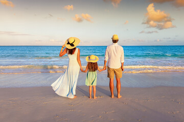 Rear view of a beautiful family standing on a beach and enjoying the view over the ocean during sunset time as a concept for travel and vacations