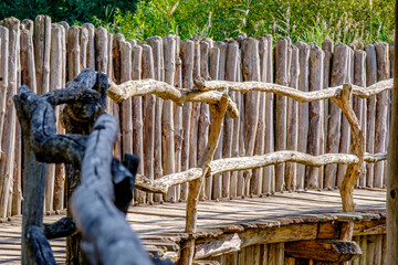 Wooden bridge connects paths in a natural setting, surrounded by greenery and rustic fencing,...