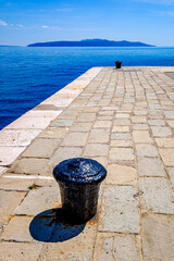 Obraz premium Dockside view of a sturdy bollard overlooking the calm blue waters, capturing a serene coastal moment in a picturesque harbor setting