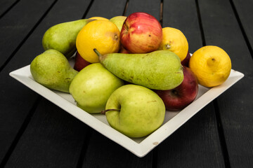 Different types of fruits on a white plate on a black wooden background