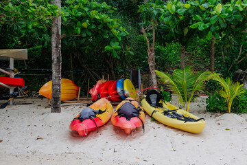 Colorful kayaks lined up on a sandy beach surrounded by lush greenery at a tropical location