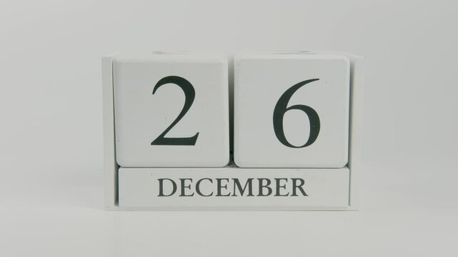 A hand flips a wooden calendar, changing the date from December 26th to December 27th, advancing through the final week of the year