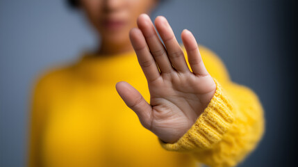 A person in a yellow sweater is extending their hand forward with an open palm in a stop gesture.

