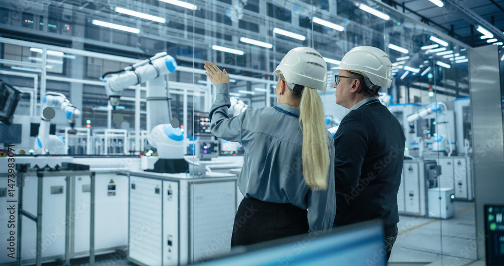 Poster Engineer and Technician Standing with Their Back to Camera, Having a Discussion and Using a Laptop Computer. Industrial Specialists Analyzing Conditions at an Electronics Factory with an Assembly Line