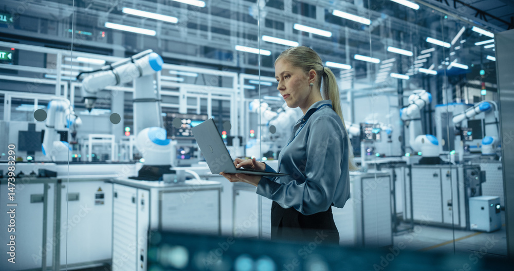 Leinwandbilder caucasian female engineer using a laptop computer to monitor robotic arms in an advanced industrial 
