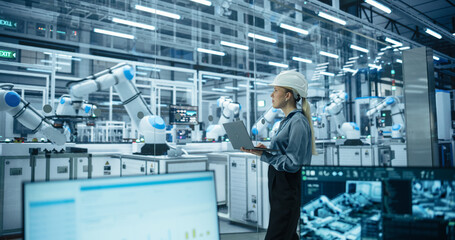 Electronics Factory Manager Working on Laptop at an Industrial Manufacture with Robotic Arms. Female Specialist Monitoring Data on a Computer, Checking and Planning Production Process