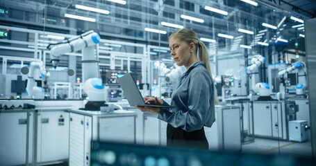 Caucasian Female Engineer Using a Laptop Computer to Monitor Robotic Arms in an Advanced Industrial...