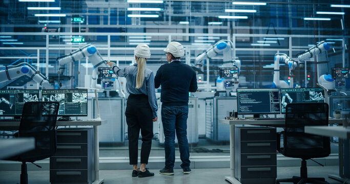 Diverse Factory Employees Using Laptop and Having a Conversation on a Production Floor. Robotic Arms Automate Electronics Assembly Inside a Facility. Automatic Conveyor is Powered by an AI Software