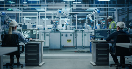 Establishing Shot at an Electronics Factory with Robotic Arms. Diverse Engineers and Developers Working on Desktop Computers
