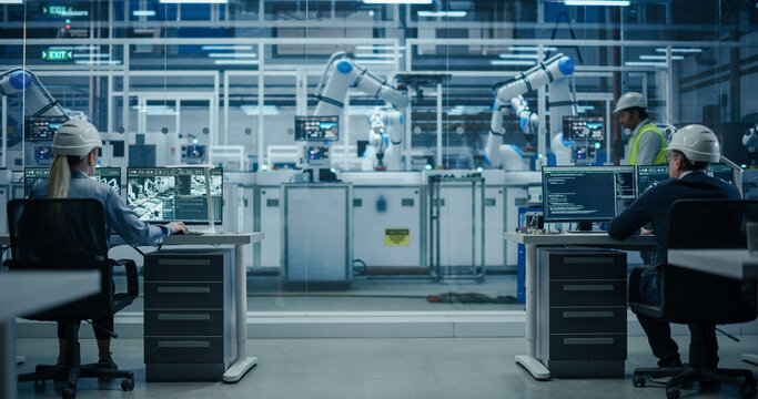 Establishing Shot at an Electronics Factory with Robotic Arms. Diverse Engineers and Developers Working on Desktop Computers - Powered by Adobe