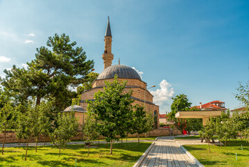 Slender minaret and domed Mirahori Mosque rising above a tree-lined park promenade in Korça,...