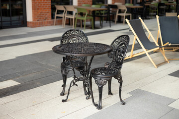 Wrought iron furniture dining table and chairs kept outside on a tiled floor at a cafe.