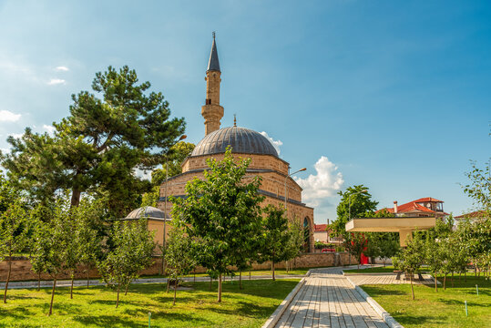 Slender minaret and domed Mirahori Mosque rising above a tree-lined park promenade in Kor&ccedil;a, Albania beneath a cloud-dappled summer sky