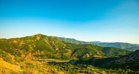 Panoramic vista of Rruga Egnatia (Via Egnatia) winding through verdant mountain valleys and...