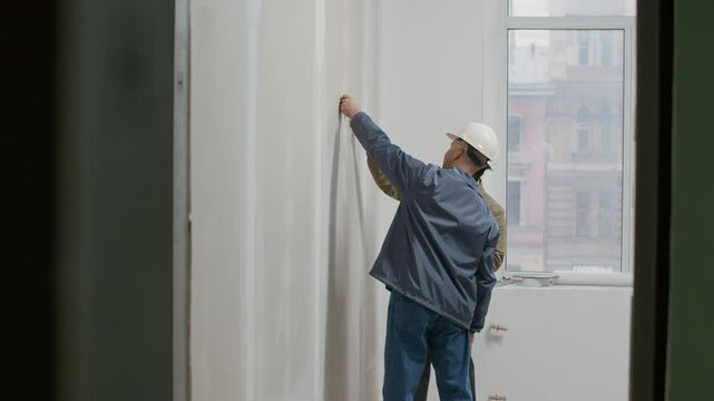 Wide shot of two bicultural engineers choosing wall color while working on site in unfinished office space