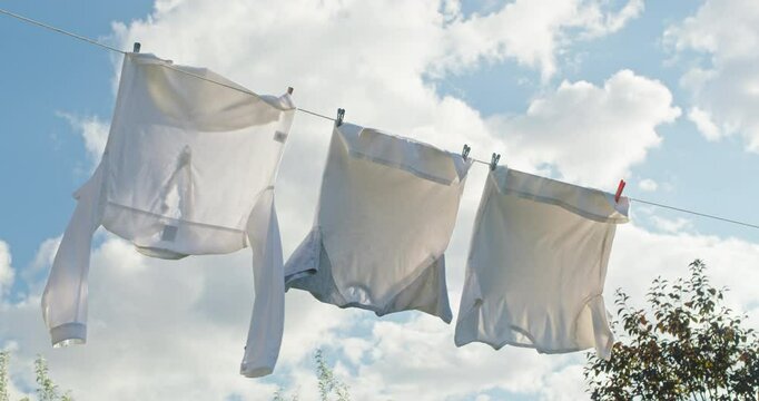 Freshly washed white clothes drying on a clothesline in the sunlight against a blue sky with clouds