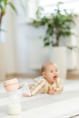 Fototapeta premium Electric breast pump with baby in background. Baby care concept.