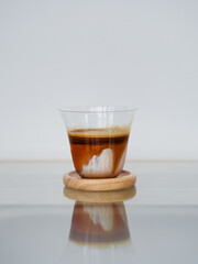 Dirty Coffee. A glass of specialty signature coffee called Dirty Coffee served on the wooden saucer. The refelction of coffee on the glass table and isolated on a white background.