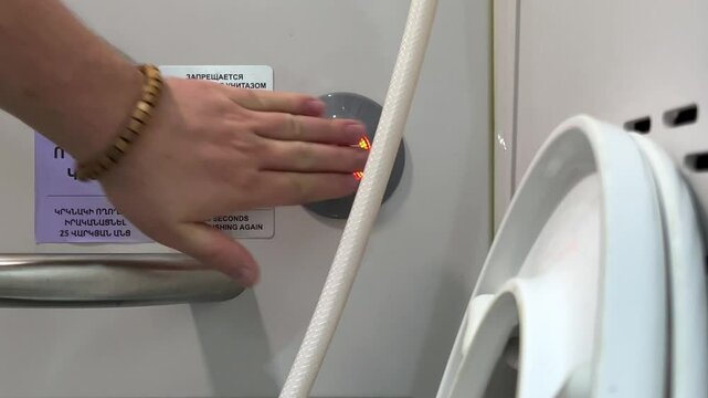 Horizontal video. Public restroom on long distance train. Male hand presses touch flush button with led lamp. Text on wall. Translation from Armenian and Russian: Do not use toilet when light is red