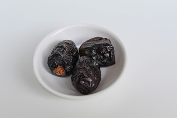 Three pieces of ajwa dates or ajwa khajur, in small bowl, isolated on white background