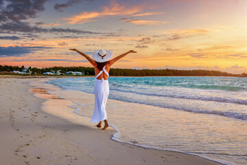 A happy woman in a white dress on vacations enjoys the beautiful sunset on a tropical paradise beach in the Caribbean Sea