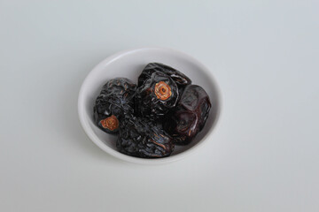 Five pieces of ajwa dates or ajwa khajur, in small bowl, isolated on white background