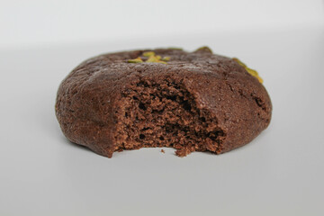 A bitten chocolate soft cookie, with green pistachio topping, isolated on white background