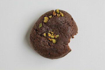 A bitten chocolate soft cookie, with green pistachio topping, isolated on white background, flat lay or top view