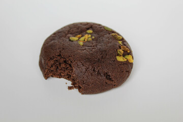 A bitten chocolate soft cookie, with green pistachio topping, isolated on white background