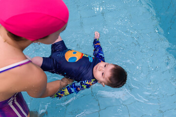 Swimming instructor holding baby floating in water during early stimulation class