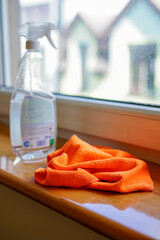 Spray bottle and orange microfiber cloth on a windowsill ready for cleaning. Close-up of a spray...