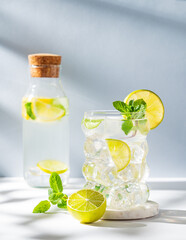 Mojito cocktail in a glass with lime, mint and ice on a white blue background with shadow and bottle.