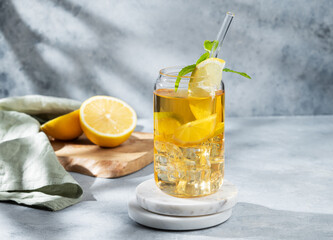 Iced drink with lemon and mint in a glass on a marble stand on light background with shadows