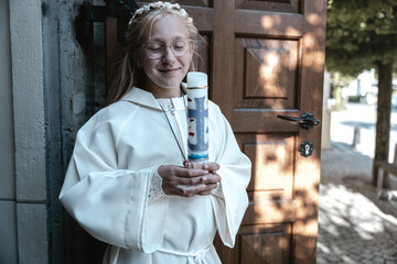 German child in white dress holding candle during First Communion in sacred church