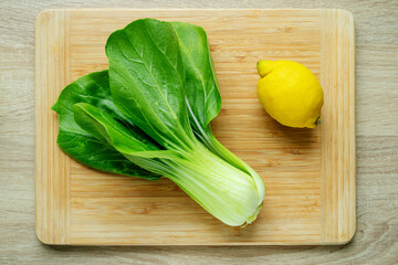 Cut green pak choi cabbage leaves and fresh lemon on wooden board. Fresh Chinese cabbage pak choi in the process of cooking. Top view.